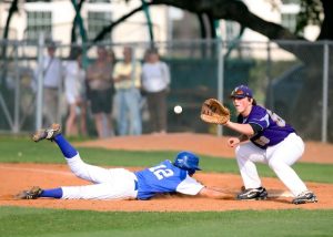 baseball player sliding head first to base while ball is thrown to opponent at base