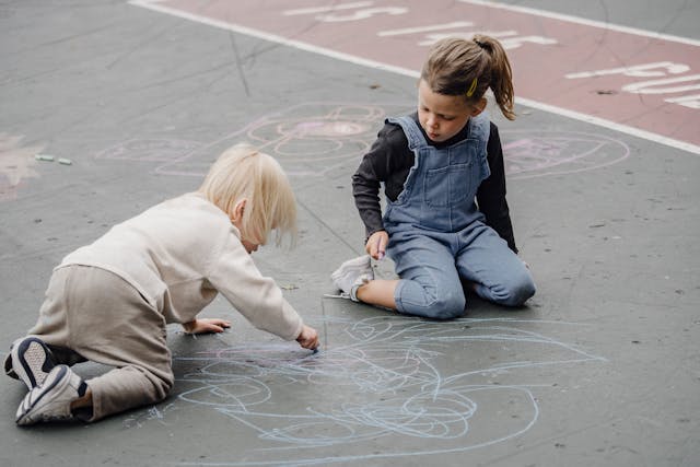 two kids drawing on pavement ground with blue chalk